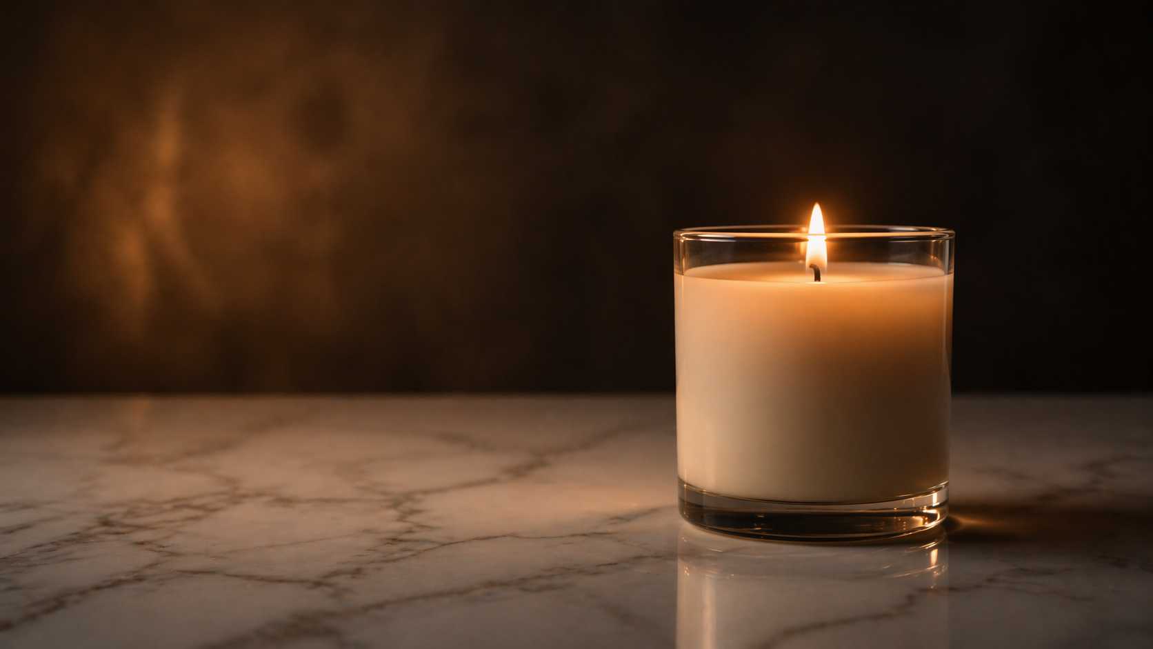 Candle in a glass holder on a marble surface with a dark background